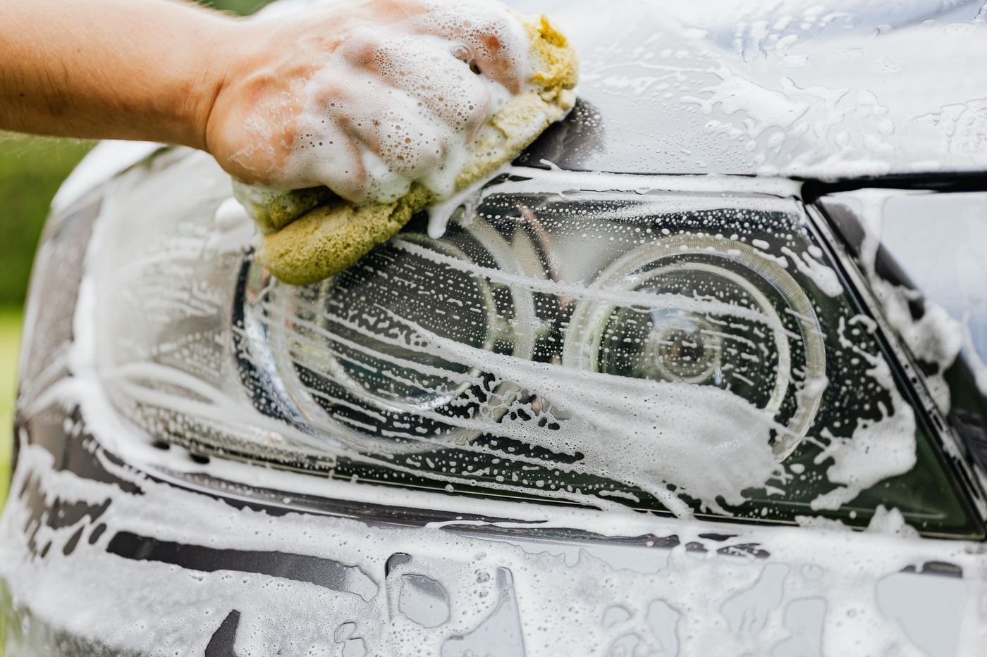 A hand working a sponge over a foamed car headlight lens