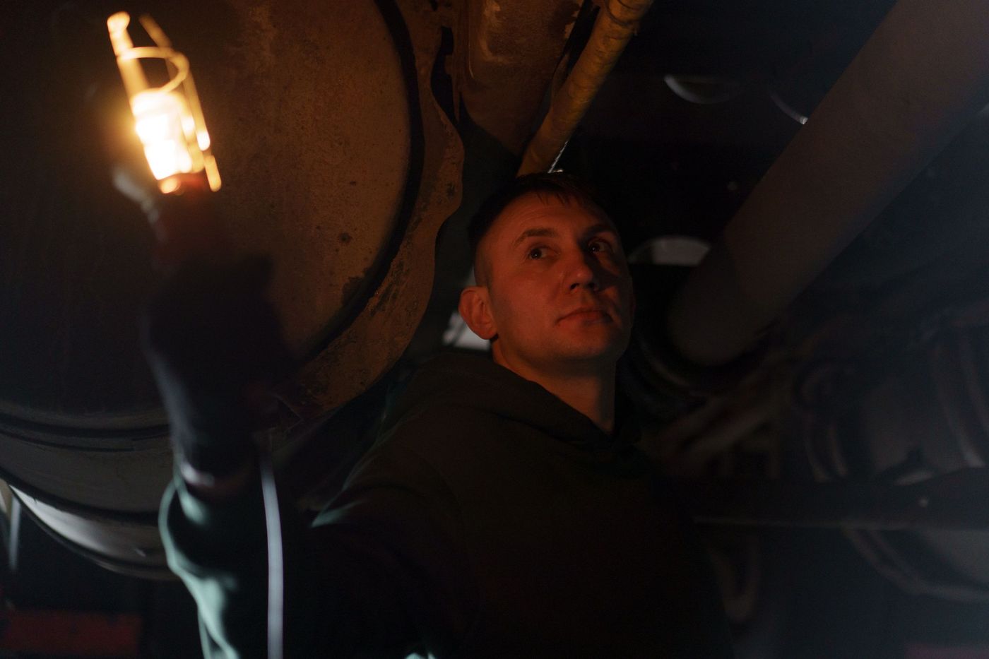 A mechanic holding a lit inspection lamp under a vehicle at night